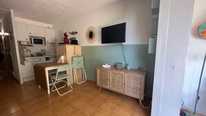 A compact kitchen with a dining area, a TV mounted on the wall, and a small cabinet. - Le tinharé - studio with garden near the sea (La Ciotat)