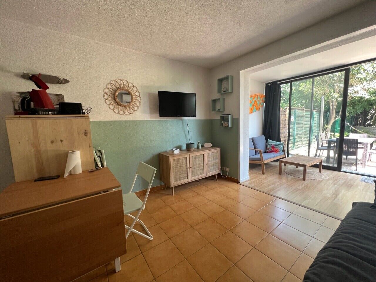 Un salon équipé d’un téléviseur, de meubles en bois, d’une armoire et d’une porte-fenêtre coulissante donnant sur un espace extérieur.