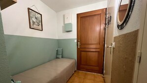 A small, narrow room with a single bed, a wooden door, and a wall-mounted mirror. - Le tinharé - studio with garden near the sea (La Ciotat)