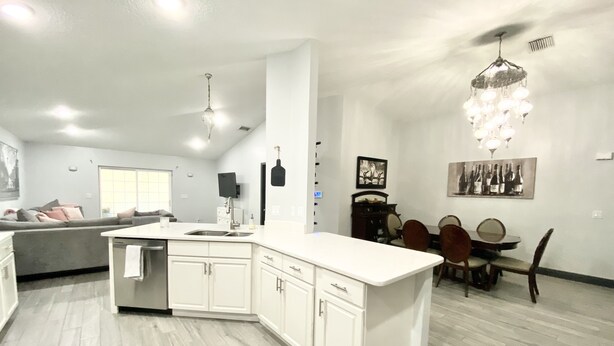 Een moderne keuken met witte kasten, een groot eiland en een eetgedeelte met een kroonluchter.