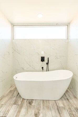 A modern bathroom with a freestanding bathtub, marble walls, and a wooden floor. - Box on the Rox Modern Container Home Heated Pool (Joshua Tree)
