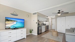 Ein modernes Wohnzimmer mit einem Flachbildfernseher, einem grauen Sofa und einer Küche im Hintergrund.