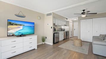 Sala de estar moderna com televisão de tela plana, um sofá cinza e uma cozinha ao fundo.