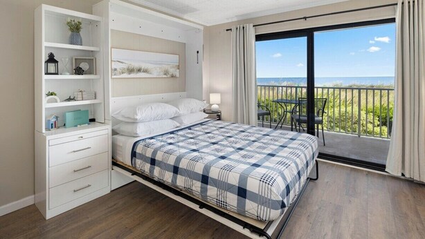 Ein Schlafzimmer mit Bett, Nachttisch, Kommode und einem Balkon mit Meerblick.