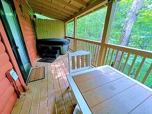 A covered deck with a table and chairs, a hot tub, and a door leading to a covered area. - Snuggle Bear: Cozy, Enchanting Mtn. Retreat Haven. New Renovated & deep cleaned! (Gatlinburg)