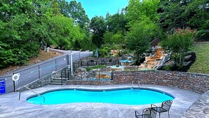 A swimming pool with a stone wall and a waterfall feature. - Snuggle Bear: Cozy, Enchanting Mtn. Retreat Haven. New Renovated & deep cleaned! (Gatlinburg)