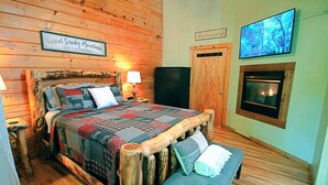 A wooden-themed bedroom with a bed, a bench, a TV, and a fireplace. - Snuggle Bear: Cozy, Enchanting Mtn. Retreat Haven. New Renovated & deep cleaned! (Gatlinburg)