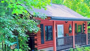 A rustic cabin with a porch, surrounded by lush greenery. - Snuggle Bear: Cozy, Enchanting Mtn. Retreat Haven. New Renovated & deep cleaned! (Gatlinburg)