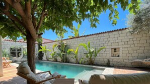 A poolside area with wooden deck, lounge chairs, and a brick wall. - Armi Alaçatı (Cesme)