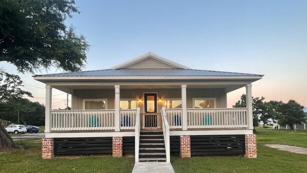 A two-story house with a front porch, a staircase leading to the entrance, and a driveway. - BRAND NEW Beach House with Gulf Views! Less than 3 min walk to the beach! (Gulfport)