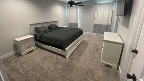 A bedroom with a bed, nightstands, a wardrobe, a ceiling fan, and a TV mounted on the wall. - BRAND NEW Beach House with Gulf Views! Less than 3 min walk to the beach! (Gulfport)