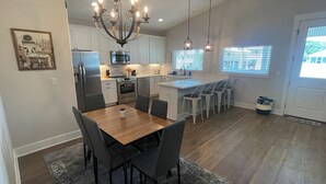 A modern kitchen with a dining area, featuring a chandelier, white cabinets, and a large island with bar stools. - BRAND NEW Beach House with Gulf Views! Less than 3 min walk to the beach! (Gulfport)