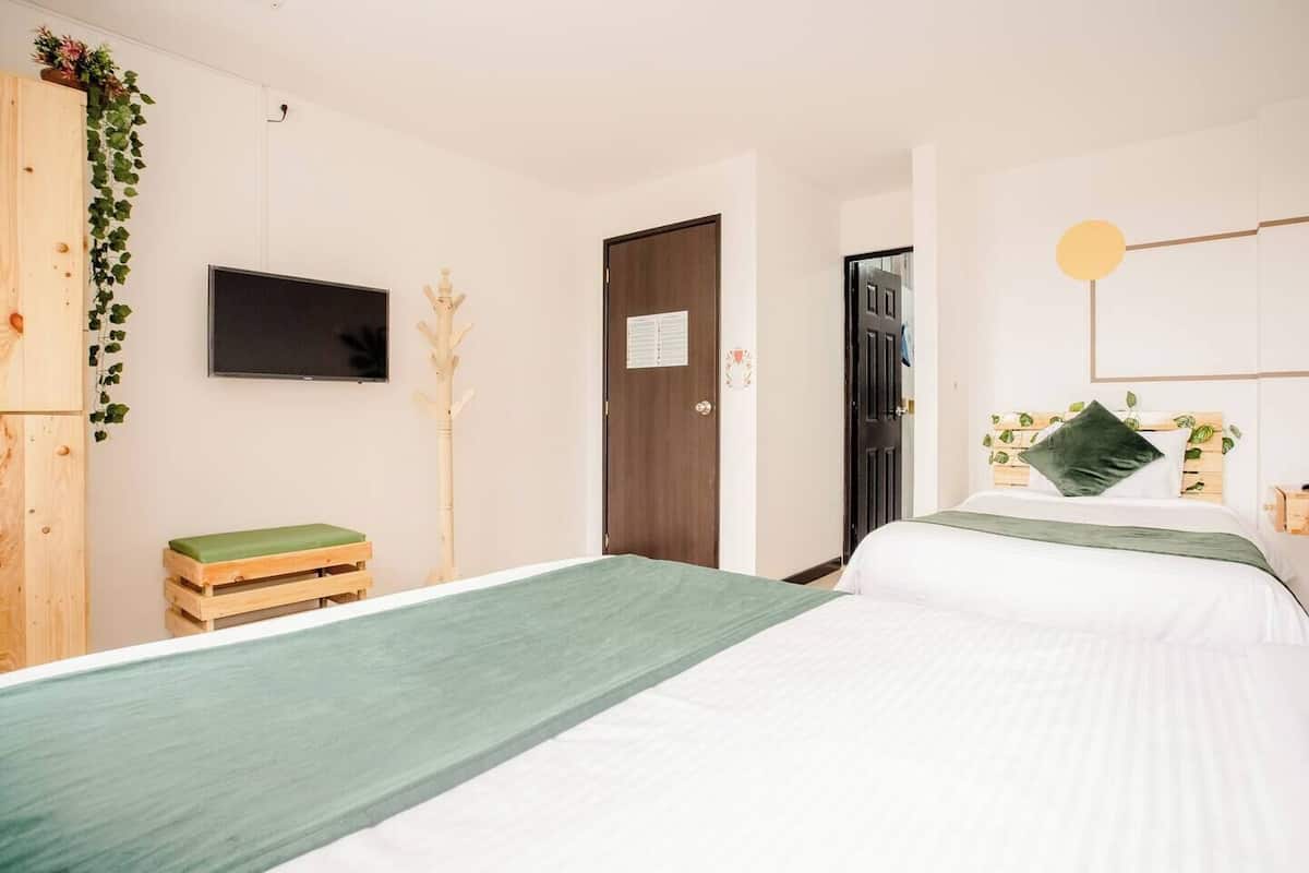 A bedroom with a bed, a TV, a wooden wardrobe, a bench, and a door.