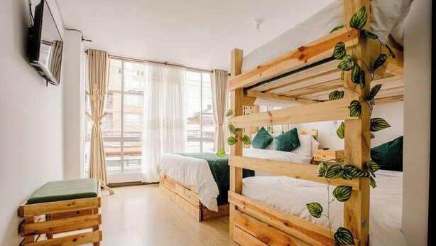 A bunk bed room with a wooden headboard, a small bench, and a window with curtains. - Hotel Natural Sevgi (Bogotá)