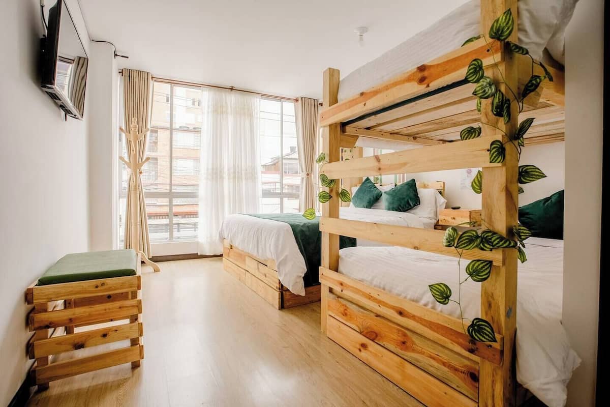 A bunk bed room with a wooden headboard, a small bench, and a window with curtains.