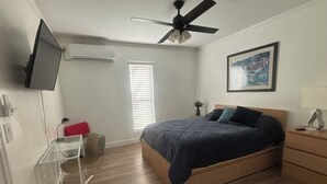 A bedroom with a bed, a ceiling fan, a TV, a desk, and a window with blinds. - Cozy In-Law Suite in South Lakeland (Lakeland)