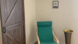 A room with a wooden sliding door, a teal chair, and a trash can. - Cozy In-Law Suite in South Lakeland (Lakeland)