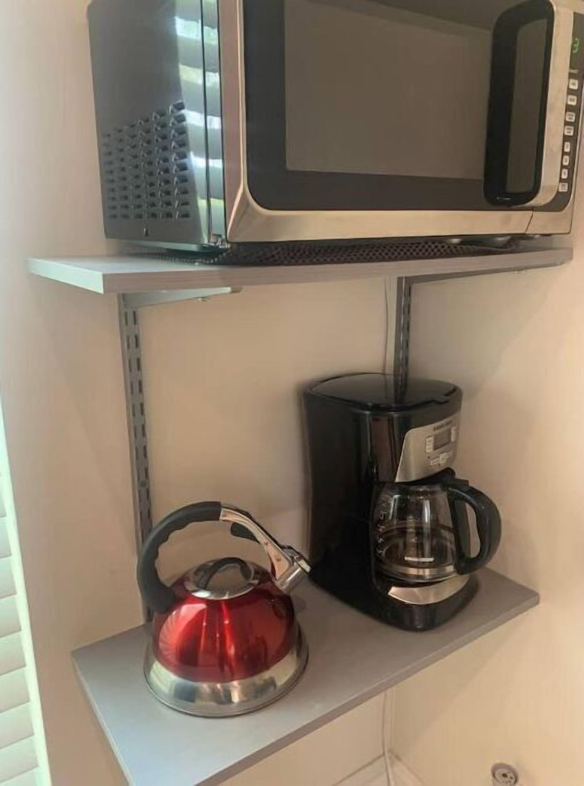 A kitchen with a microwave, a coffee maker, and a kettle on a shelf.