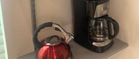 A kitchen with a microwave, a coffee maker, and a kettle on a shelf.
