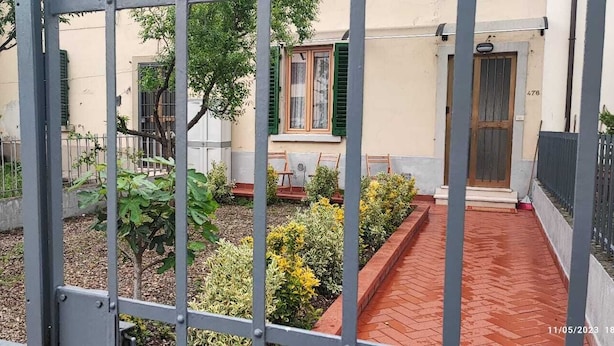 Un patio con sendero de ladrillo, cerca de metal y un edificio con puerta y ventana.