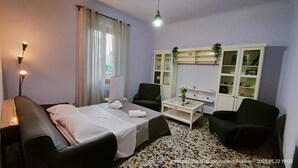 Habitación de hotel con cama, dos sillones, una mesita, un aparador con puertas de vidrio y una ventana con cortinas.