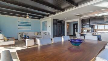Un espacio habitable amplio con un gran comedor de madera, muebles blancos y una cocina al fondo.