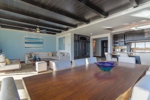 Un vaste espace de vie comprenant une grande table à manger en bois, des meubles blancs et une cuisine située à l’arrière-plan.