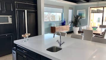 Una cocina moderna con una isla grande, armarios oscuros y un lavamanos de acero inoxidable.