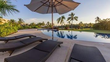 Un área junto a la piscina con sillones de descanso y una sombrilla.