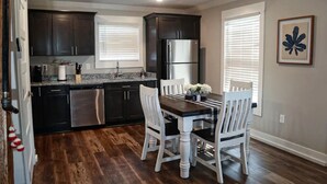 Una cocina moderna con armarios oscuros, electrodomésticos de acero inoxidable y una mesa de comedor de madera con sillas blancas.