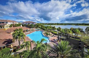 Un complexe hôtelier doté d’une grande piscine entourée de palmiers et de chaises longues, offrant une vue sur un lac.