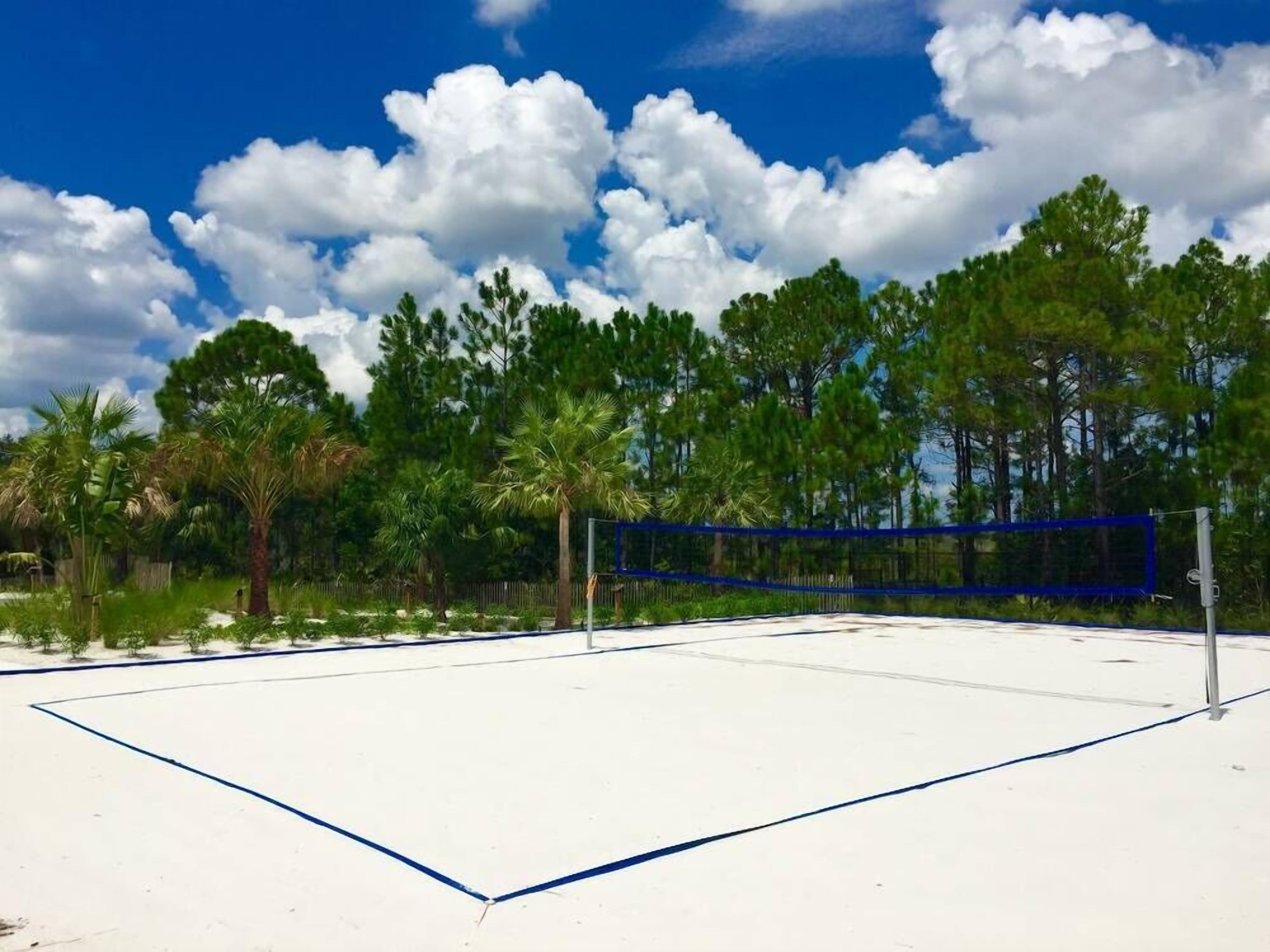 Cancha de tenis con red, rodeada de árboles y un cielo despejado.