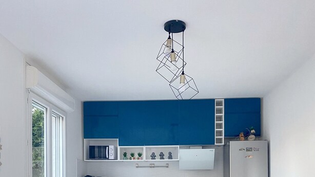 A modern kitchen with blue cabinets, a white refrigerator, and a dining table with colorful chairs. - Maison Sécurisée à 2km de la Plage et du Centre-ville (Soulac-sur-Mer)