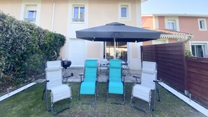 A patio with four lounge chairs, a table, and a large umbrella. - Maison Sécurisée à 2km de la Plage et du Centre-ville (Soulac-sur-Mer)