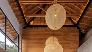 A modern living room with a high ceiling, wooden beams, and large woven pendant lights.