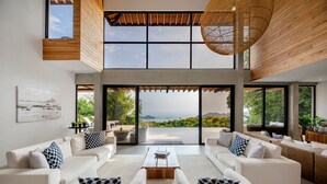 A spacious living area with a large window overlooking a scenic view, a high ceiling with wooden beams, and a modern design.