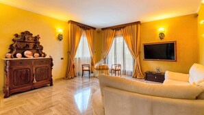 Un soggiorno con un divano, un mobiletto in legno con oggetti decorativi, una TV montata a parete e due poltrone.