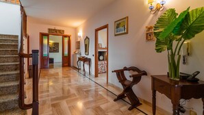 Un corridoio con una scala in legno, una panca di legno, una pianta in vaso e opere d'arte appese alle pareti.