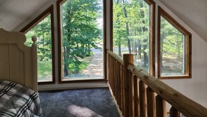 A bedroom with a large skylight, a wooden railing, and a plaid bedspread.