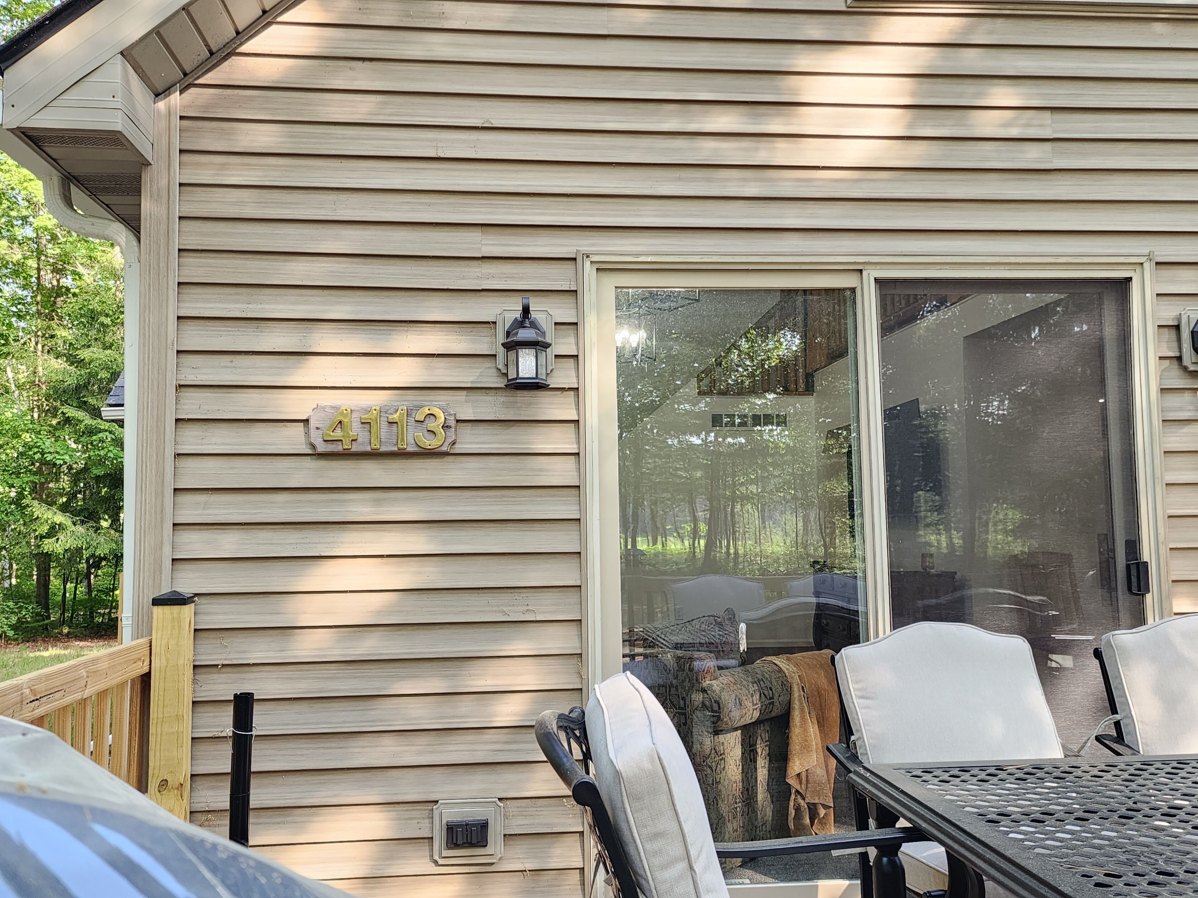 A wooden house with a sliding glass door, a mailbox with the number 4113, and outdoor furniture.