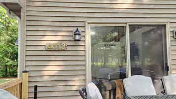 A wooden house with a sliding glass door, a mailbox with the number 4113, and outdoor furniture.