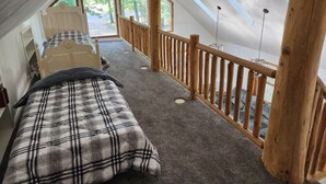 A bedroom with a loft bed, a wooden railing, and large windows offering a view of trees.
