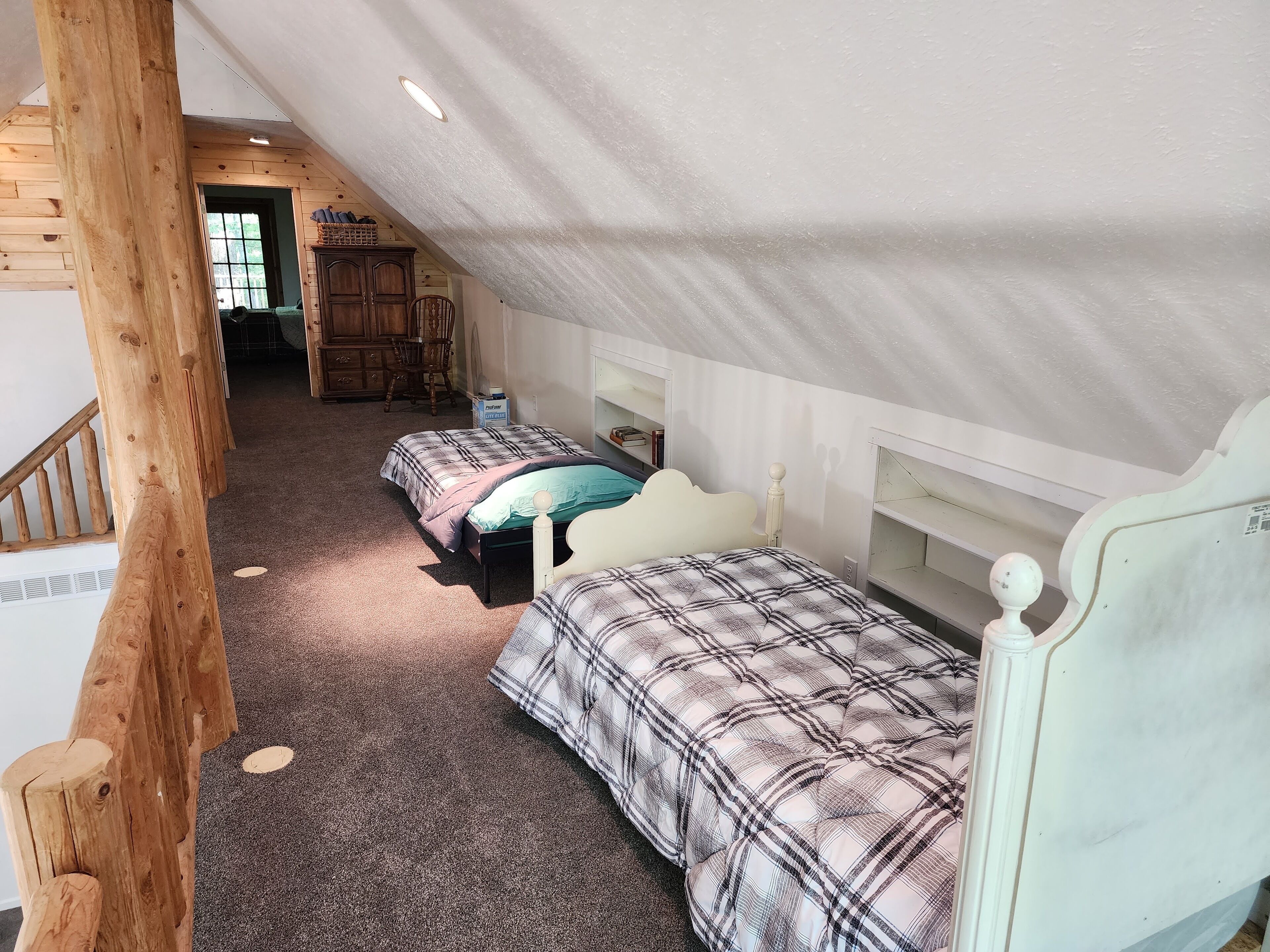 A bedroom with two beds, a wooden staircase, and a loft area with a desk and chair.