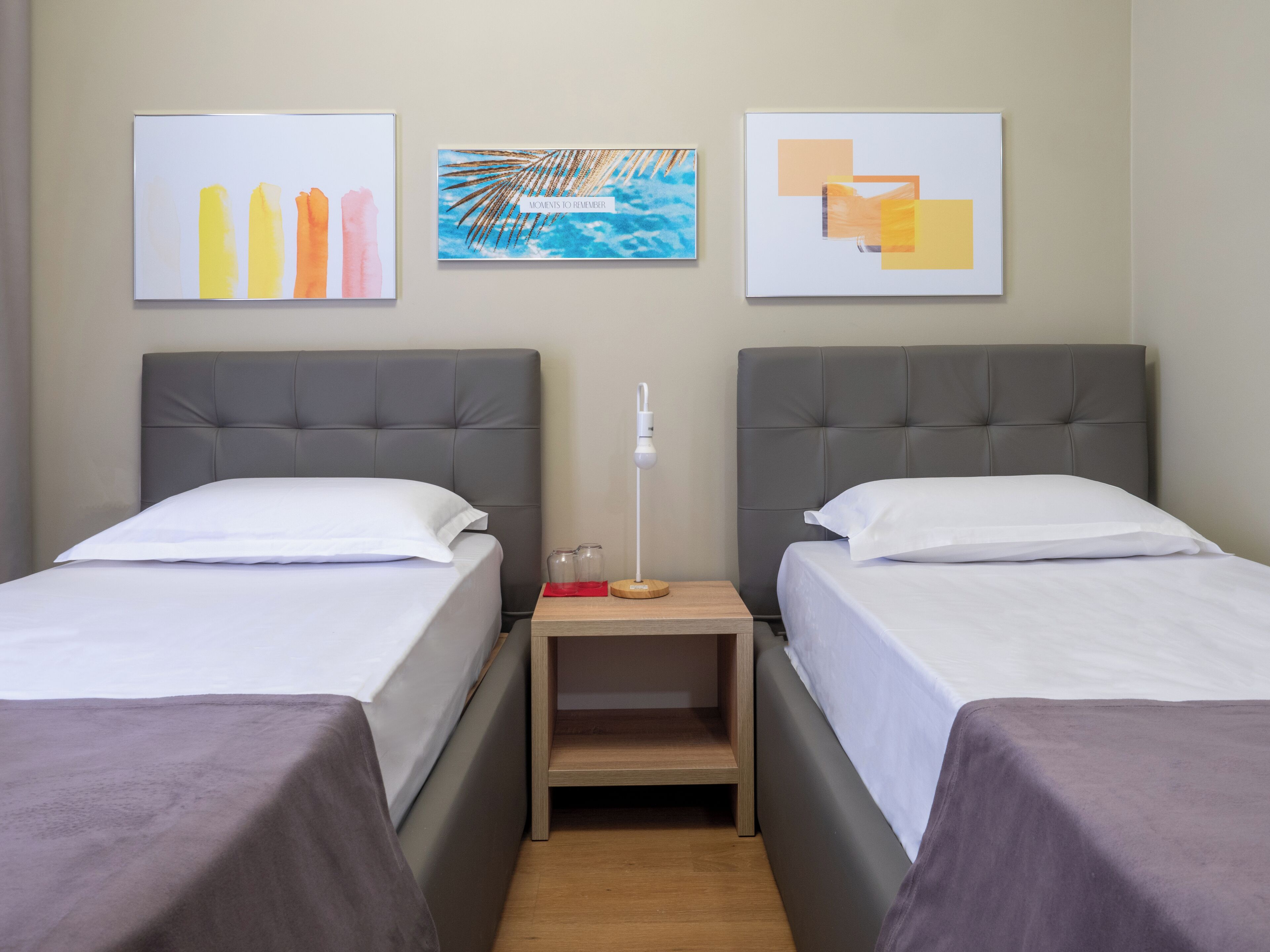 A hotel room with two beds, a nightstand, and three wall-mounted artworks.