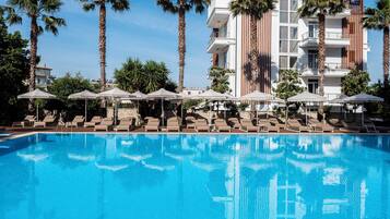 Relax by the rectangular pool surrounded by lounge chairs and umbrellas, amidst lush greenery and tropical ambiance.