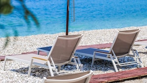 A beach with two sun loungers and a white umbrella, a pebble beach, and a clear blue sea. - Nia Boutique Hotel by Rapos Resort (Himarë)
