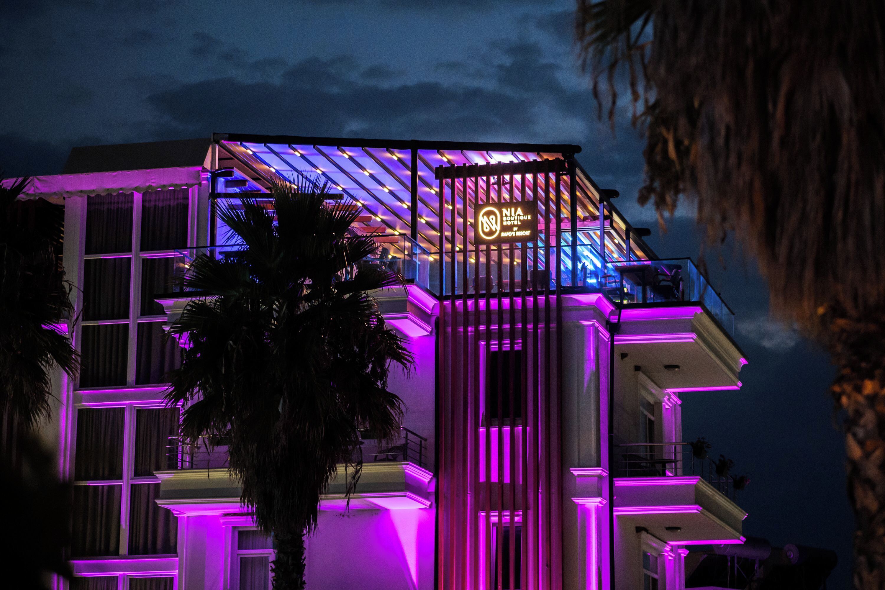 A hotel with a modern design, featuring a prominent neon sign and a balcony with a view.