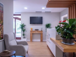A modern hotel lobby with a sofa, a wooden reception desk, a television, and potted plants. - Nia Boutique Hotel by Rapos Resort (Himarë)