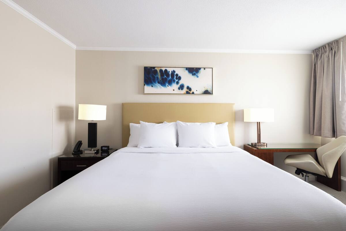 A hotel room with a large bed, two bedside tables with lamps, a desk, and a chair.