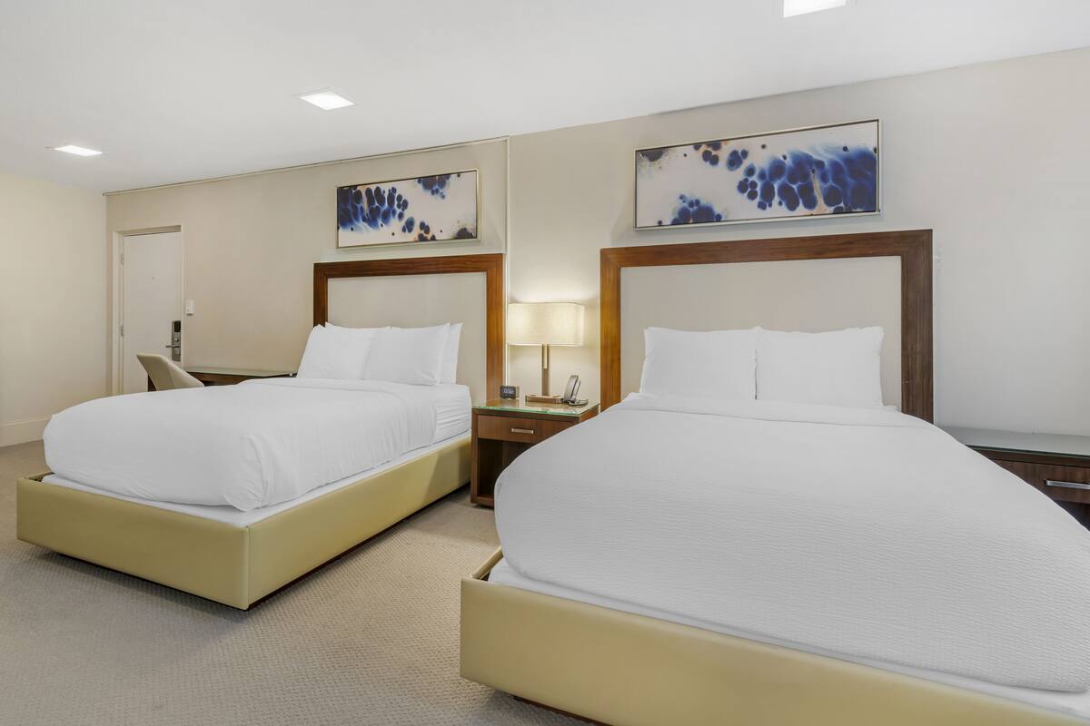 A hotel room with two beds, a nightstand with a lamp, and abstract wall art.